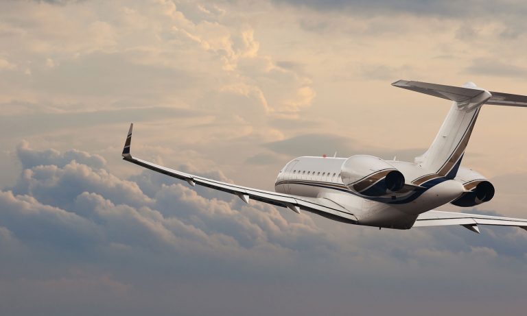 White private jet with brown and black stripe flying in overcast sky